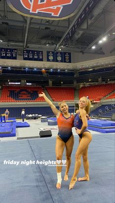 two women standing on top of a blue and red floor in front of an arena