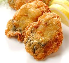 some fried food is on a white plate with lemon wedges and a slice of apple