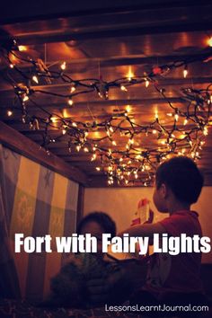 two children are sitting on a bed with fairy lights hanging from the ceiling above them