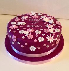 a birthday cake with pink and white flowers on the top is sitting on a purple plate