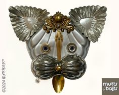 a silver mask with gold accents on it's face and eyes is hanging from a wall