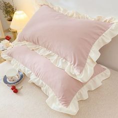 two pink pillows sitting on top of a bed next to a cup and saucer