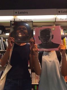 two people holding up posters in front of bookshelves, one with a man's face on it