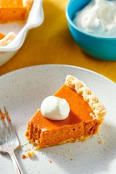 a slice of pumpkin pie on a white plate with a fork and bowl in the background