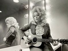 a woman sitting in front of a mirror playing a guitar