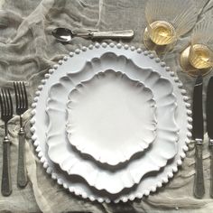 an empty white plate with silverware on a tableclothed cloth, next to utensils and spoons