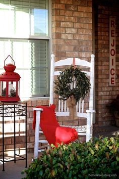 a white rocking chair sitting on top of a porch next to a red lantern and wreath