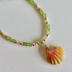 Hawaiian Sunrise Shell Necklace~ This necklace has a beautiful orange, pink, green wire wrapped Hawaiian sunrise shell with small pink faceted opals, green peridot chip gemstones and gold beads for accent. Sunrise shells are only found in Hawaii, a true gem to the islands and collectors.  Shell approx. .75" Necklace is adjustable 16- 18" Model wearing similar necklaces Checkout our sunrise shell jewelry~ https://www.etsy.com/shop/HanaMauiCreations?ref=seller-platform-mcnav&search_query=sunrise+shell+jewelry SHOP~  http://www.etsy.com/shop/HanaMauiCreations?ref=si_shop International buyers please read our shipping policies before ordering~ POLICIES~ https://www.etsy.com/shop/HanaMauiCreations/policy?ref=shopinfo_policies_leftnav Surfer Girl Gifts, Sunrise Shell, Tahitian Pearl Necklace, Necklace Gold Chain, Crystal Point Necklace, Black Pearl Necklace, Hawaii Beach, Peridot Gemstone, Green Peridot