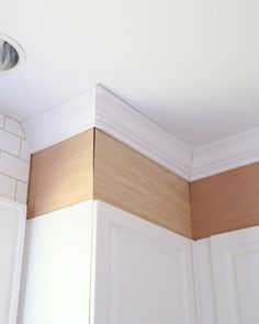 the corner of a kitchen with white cabinets and wood trim on the wall above it