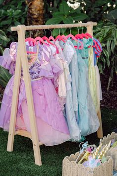 a rack full of dresses sitting on top of a grass covered field next to a basket