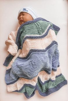 a baby wrapped up in a blanket on top of a white sheet with a blue and green stripe