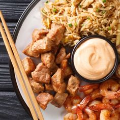 a plate with shrimp, rice and chopsticks next to a bowl of dipping sauce