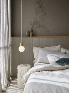 a bed sitting under a window next to a lamp on a wooden headboard in a bedroom