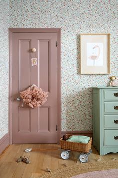 a baby's room with a pink door and floral wallpaper