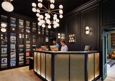 the front desk of a hotel lobby with lights hanging from it's ceiling and bookshelves in the background