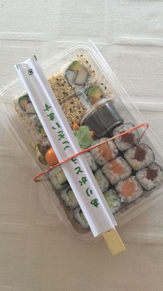 a plastic container filled with sushi and chopsticks on top of a table