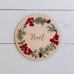 a wooden plaque with the word noel surrounded by red flowers and pine cones on a white background