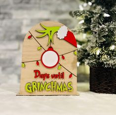 a wooden sign with the words days until grinmas on it next to a potted christmas tree