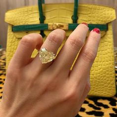 a woman's hand with a ring on it and a yellow purse in the background