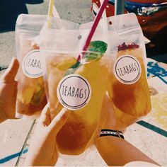 three people holding up drinks in plastic bags with straws and lemon slices on them