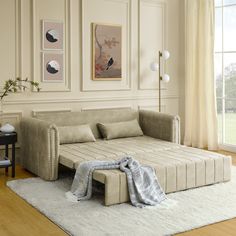 a living room with a couch, ottoman and rug in front of the window that has pictures on the wall