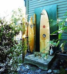 two surfboards are propped up against the side of a house in front of some bushes