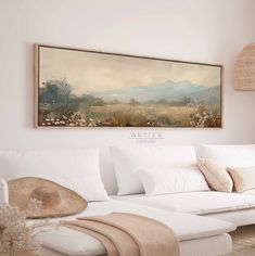 a painting hanging on the wall above a white couch in a living room with pillows