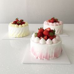 three cakes with white frosting and strawberries on top, one has pink icing