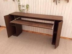 a wooden desk sitting in front of a wall with shelves on each side and plants