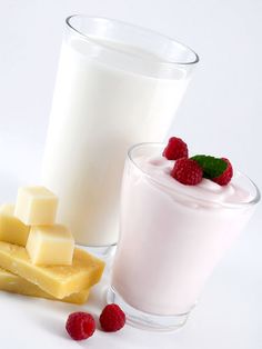 two glasses filled with milk and raspberries next to one glass full of milk