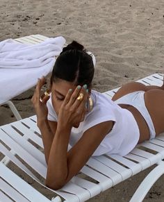 a woman laying on top of a white beach chair talking on a cell phone while holding her hand to her face