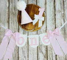 pink and white first birthday banner on wooden table with hat, cake plate and other items