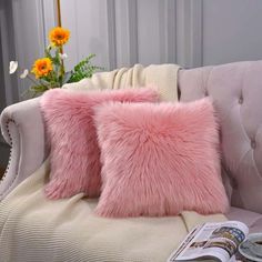 two pink pillows sitting on top of a white couch next to a vase with flowers