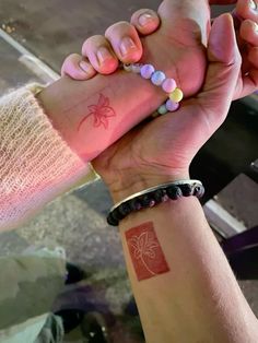 two people are holding hands with tattoos on their arms and wristbands, one has a spider tattoo on it