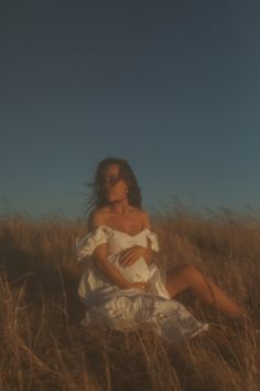 a woman in a white dress is sitting in the grass with her hands on her stomach