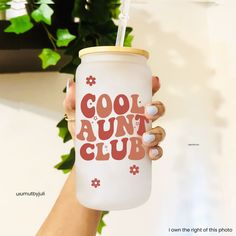 a woman holding up a white cup with the words cool aunt club on it and a straw in her hand