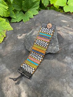 a black and white bracelet sitting on top of a rock next to green leaves in the background