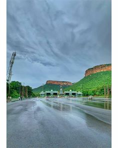 the road is wet and there are cars parked on it in front of some mountains