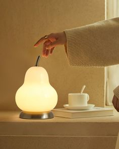 a person is lighting a small lamp on a table next to a cup and saucer