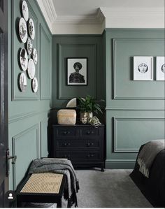 a bedroom with dark green walls and white plates on the wall above the bed, along with a black chest of drawers