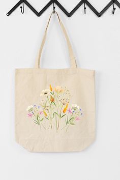 a tote bag hanging on a wall with flowers painted on the front and bottom