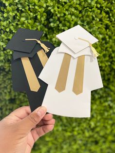 two graduation hats and gowns are being held up in front of a green hedge