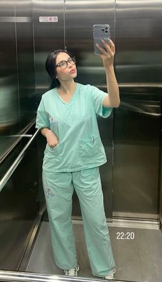 a woman in scrubs taking a selfie with her cell phone while standing on an escalator