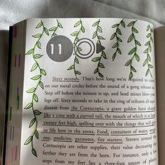 an open book with green leaves on the pages and numbers 11 in each corner, sitting on a bed sheet