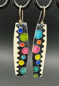 two pairs of earrings with multicolored glass beads hanging from metal hooks on a black background