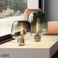 two glass lamps sitting on top of a table next to a window