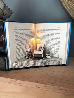 an open book sitting on top of a wooden table next to a lamp and books