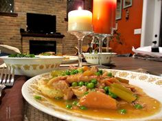 a dinner plate with meat, vegetables and sauce on the table next to a candle