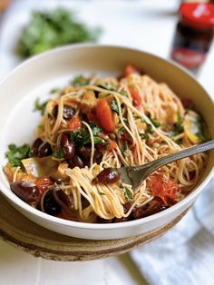 a white bowl filled with pasta and olives on top of a wooden cutting board