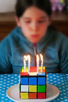 a young boy sitting at a table with a cake shaped like a rubik cube